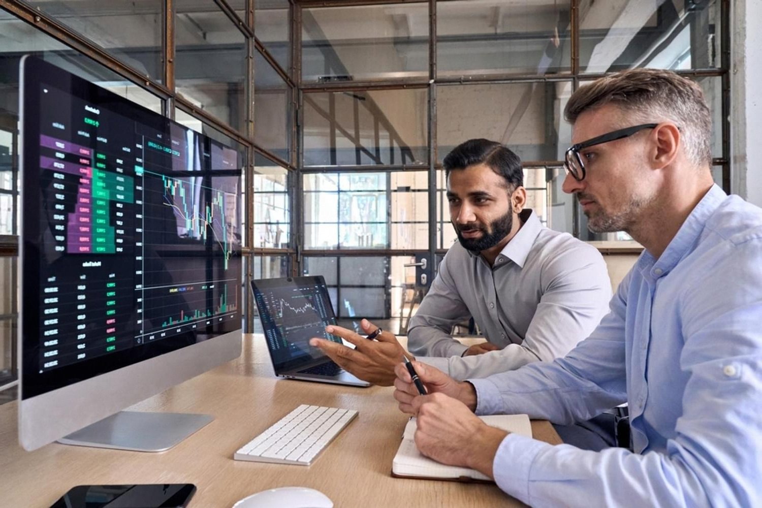 Two analysts reviewing financial controls and reports on a monitor